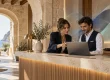 Dos profesionales revisan un portátil en la recepción de un hotel; ilustración conceptual sobre IA y venta directa.